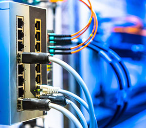 Close-up of a network switch with multiple connected Ethernet cables and orange fiber optic cables. The background is blurred, emphasizing the focus on the switch and cables, suggesting a high-tech environment such as a data center or server room where project finance supports cutting-edge infrastructure.